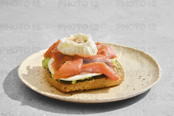 Toasted bread with smoked salmon, avocado, goat cheese and a poached egg on top. The food is garnished with spices