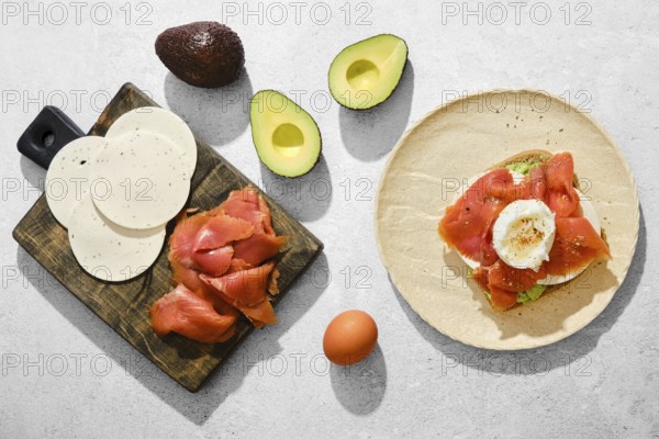 Top view of ingredients for smoked salmon sandwich with avocado, goat cheese and poached egg on a kitchen tabletop