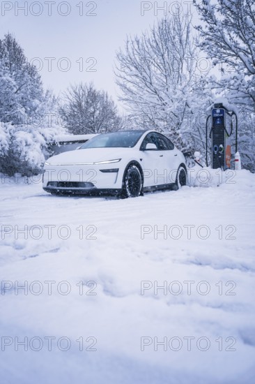 White electric car standing in a snowy landscape next to a charging station, Tesla Model Y electric car, ENBW charging station, Waldachtal, Freudenstadt district, Germany