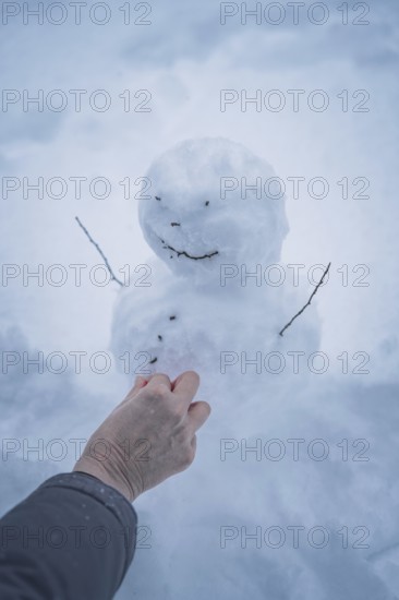 A hand shapes a small snowman in the snow, simple winter joy, Waldachtal, Freudenstadt district, Germany