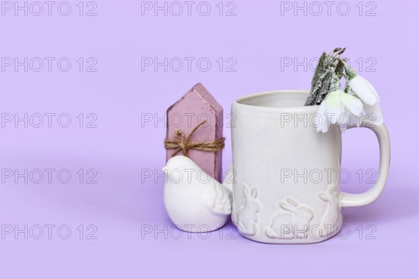 Cute spring decor arrangement with bird, tulip flowers and mug with Easter bunnies, bird and flowers on violet background with copy space