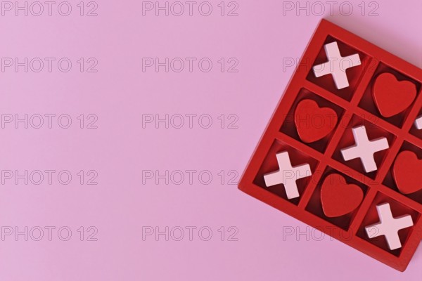 Valentine-themed heart game with red and pink hearts and Xs in a red box on a pink background with copy space
