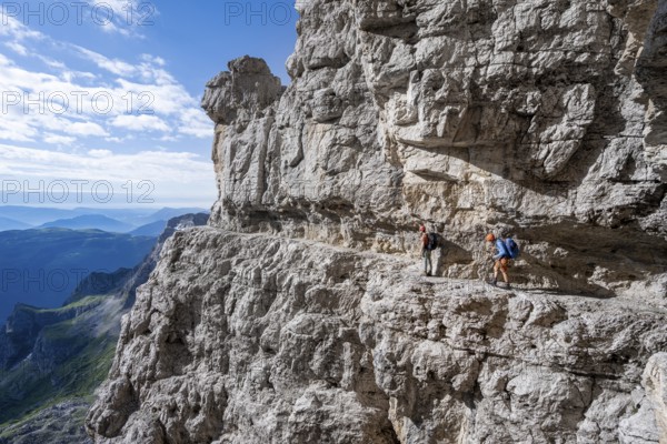 Two mountaineers on an exposed rock band in the secured via ferrata Bocciere Centrale, Brenta Mountains, Brenta-Adamello Natural Park, Trentino, Italy