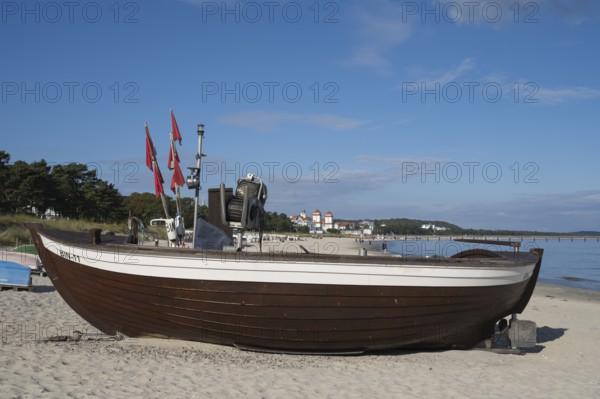 Boat with fishing flags is lying on a sandy beach, behind the spa hotel, blue sky, Binz, seaside resort, island of Rügen, Baltic Sea, Mecklenburg-Western Pomerania, Germany