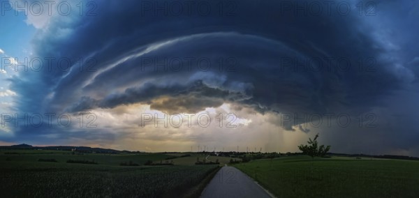 Supercell, approaching thunderstorm with impressive and threatening cloud formation of a thunderstorm over a village with wind turbines in the background, Baden-Württemberg, Germany