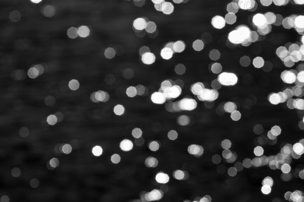 Abstract black background, sparkling white lights, bokeh balls, light reflections on water surface, octagonal light spots, copy space, background image, Sicily, southern Italy, Italy