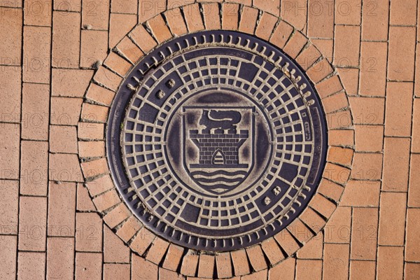 Manhole cover, city coat of arms, paving brick footpath, sunny, Eckernförde, Rendsburg-Eckernförde district, Schleswig-Holstein, Germany