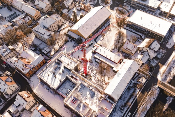 Bird's eye view of snow-covered city with construction crane and surrounding buildings in warm sunlight, Neubau Zellerschule, Nagold, Black Forest, Germany