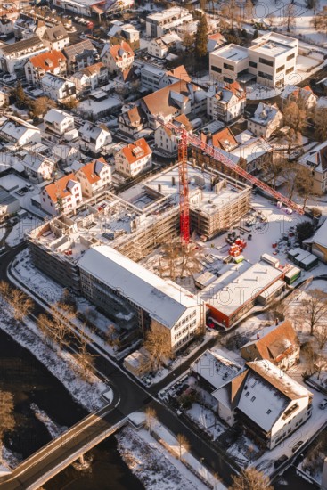 Construction site in a snowy urban area with a visible red construction crane, Zellerschule building, Nagold, Black Forest, Germany