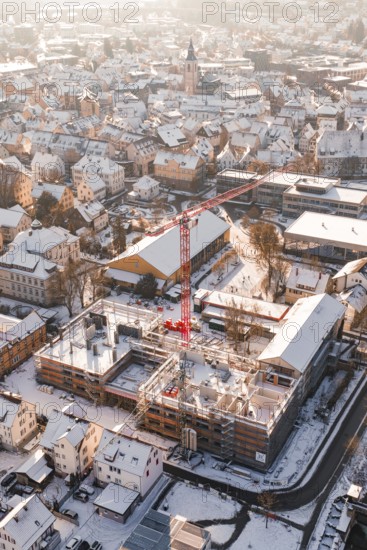 City view in winter with snow-covered roofs and a red construction crane in front of a snowy landscape, Neubau Zellerschule, Nagold, Black Forest, Germany
