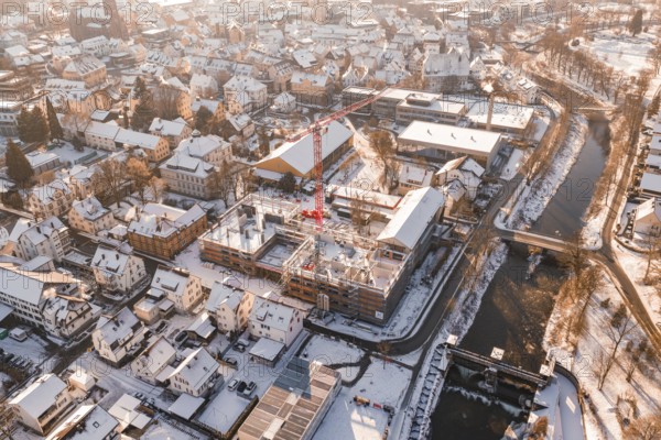 Snowy town with red construction crane standing on a construction site near a river, Zellerschule building, Nagold, Black Forest, Germany