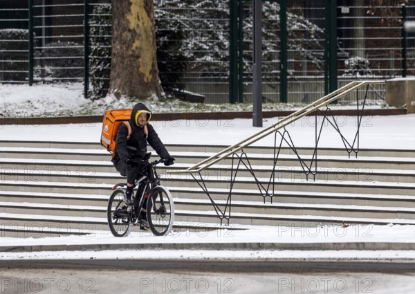 Winter in Stuttgart. There is a closed blanket of snow in the city center. Lieferando cyclists in front of the stairs at the city palace. Stuttgart, Baden-Württemberg, Germany