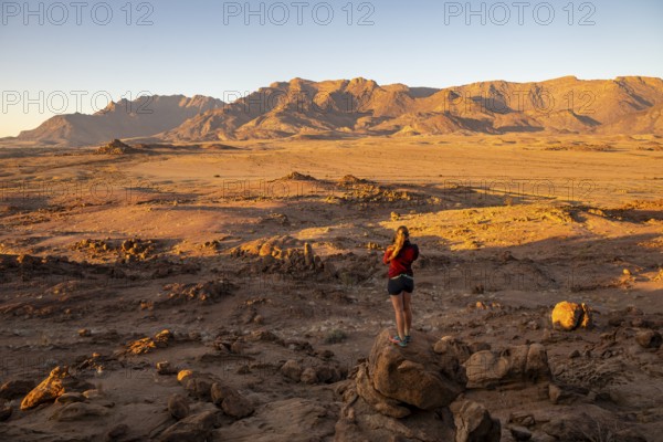 Young woman standing in desert landscape with Brandberg in morning light, at sunrise, Erongo, Damaraland, Namibia