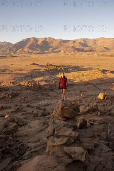 Young woman standing in desert landscape with Brandberg in morning light, at sunrise, Erongo, Damaraland, Namibia