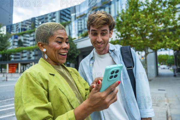 Diverse colleagues standing in a city, happily sharing and viewing content on a smartphone, representing connection, joy, and successful urban business collaboration