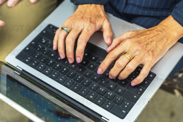 Mature womans hands with painted nails and rings typing on a laptop keyboard, close up conveying remote work, business communication, productivity and professional digital connection