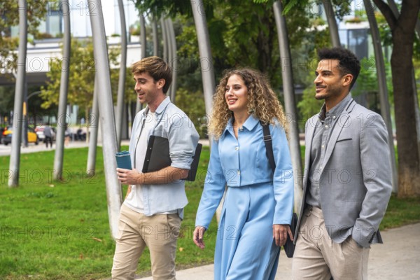 Three diverse business professionals, two men and one woman, walking and conversing outdoors in a modern urban park setting, representing teamwork, collaboration, and a dynamic work environment