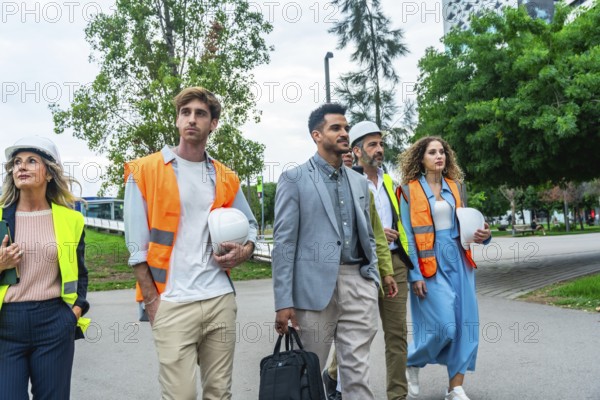 Group of diverse construction professionals and architects wearing hard hats and safety vests, walking purposefully through an urban park, discussing future projects and teamwork