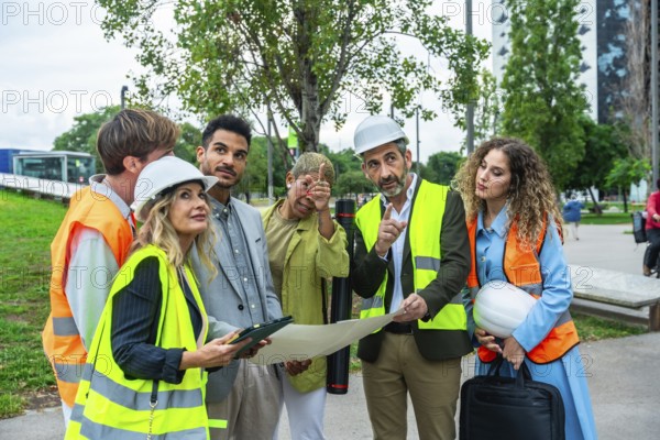 Architects, engineers, and construction colleagues in hard hats and vests discussing blueprints and development plans while surveying an urban environment project site
