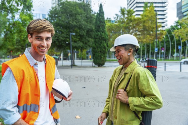 Diverse team of architects and engineers smiling and talking while standing outdoors in the city, carrying their safety helmets and blueprints, representing collaboration and urban development