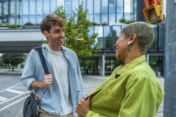 Two diverse business colleagues laugh and chat while walking on a city street, sharing a friendly, collaborative moment amid modern architecture and urban professional life