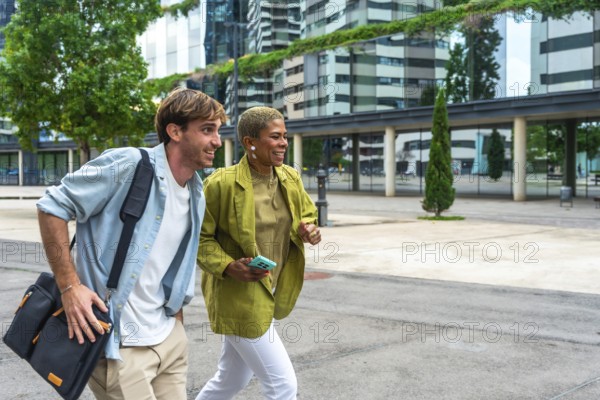 Diverse business professionals walking and discussing in a modern urban area, holding a bag and phone, reflecting concepts of teamwork, commuting, and dynamic city life