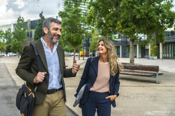 Professional man and woman walking outdoors in a modern urban environment, having a conversation and smiling, representing teamwork, collaboration, and successful business partnership