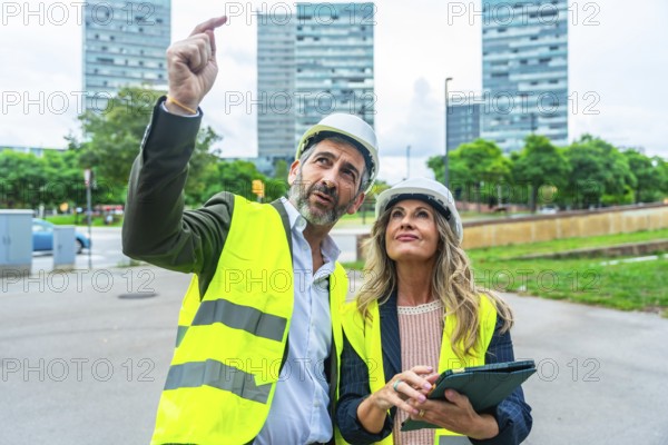 Male and female architects or engineers wearing hard hats and high visibility vests inspecting a new urban development with towering buildings under construction in the background