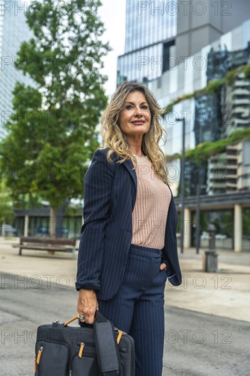 Confident businesswoman wearing a pinstripe suit, holding a briefcase and looking forward, standing outdoors against a modern urban building with green features implying sustainability