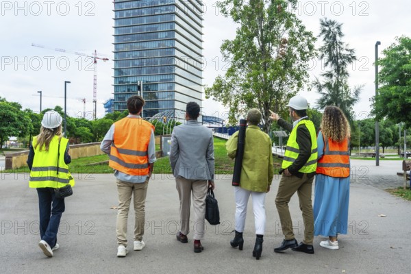 Diverse group of architects, engineers, and construction professionals walking and discussing plans near a modern building and active urban development project
