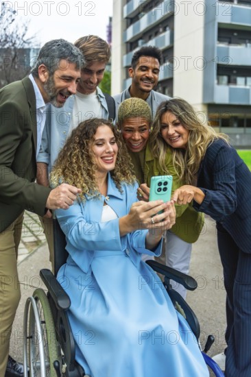 Diverse group of professional colleagues, including a woman in a wheelchair, smiling and interacting around a mobile phone, embracing inclusion and technology in an urban setting