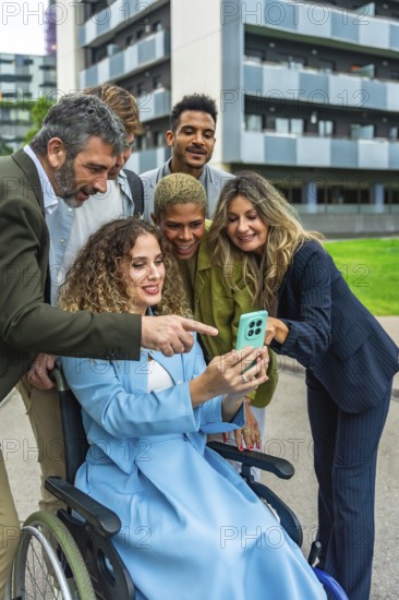 Multi ethnic business team smiling and reviewing a corporate project on a smartphone held by a woman in a wheelchair, showcasing teamwork, inclusion and modern urban collaboration
