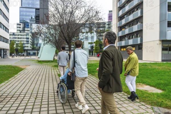 Diverse group of colleagues walking on a paved pathway through a modern city district, one person pushing a colleague in a wheelchair, symbolizing inclusivity and teamwork