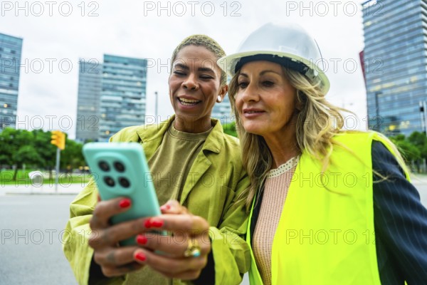 Diverse women architects and engineers smiling and collaborating outdoors in a modern city, using a smartphone for teamwork and communication on a construction project