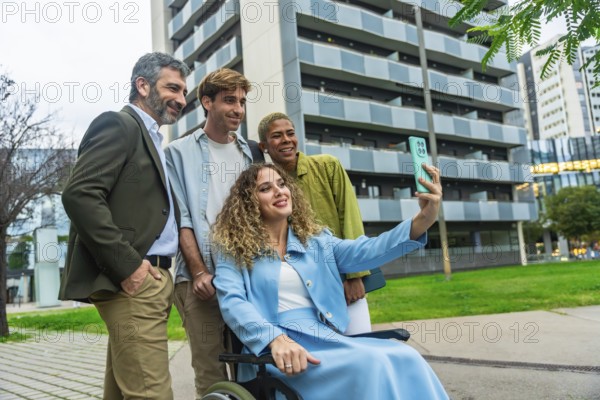 Diverse group of smiling business colleagues, including a woman in a wheelchair, capturing a selfie together with a smartphone outdoors in a modern city setting