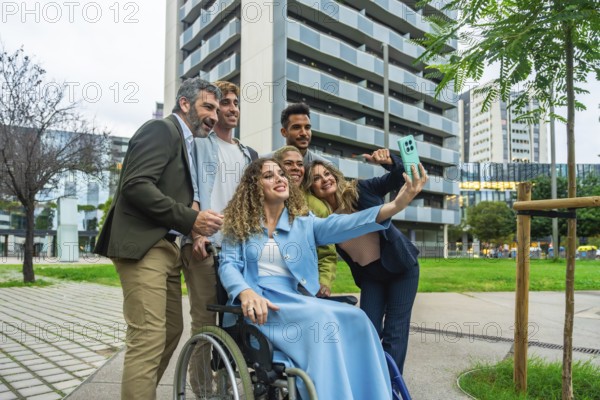 Diverse group of business colleagues, including a woman in a wheelchair, smiling and taking a selfie with a smartphone outdoors in a city setting, showcasing teamwork and inclusion