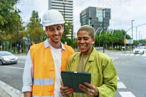 Construction manager man in hard hat and woman architect reviewing building plans on a digital tablet, collaborating on a project in an urban environment