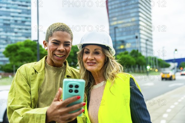 Diverse women architects and engineers smiling outdoors, looking at a smartphone screen, collaborating on an urban construction project, symbolizing teamwork, technology, and success in the city