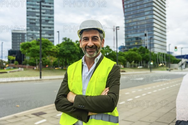 Senior construction professional in hard hat and high visibility vest stands with arms crossed, confident smile, city skyline behind him symbolizing urban development and leadership