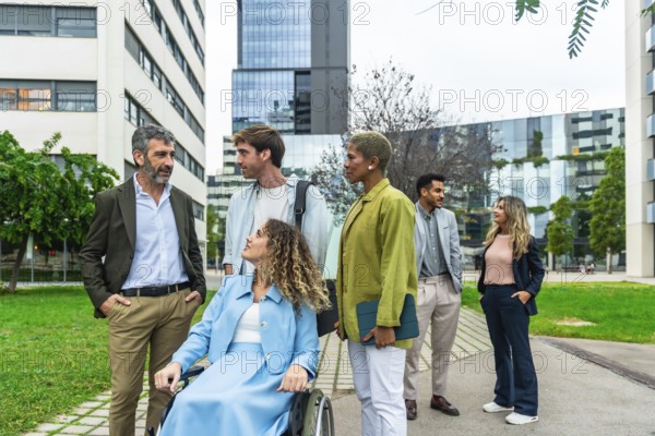 Group of diverse business professionals, including a woman using a wheelchair, collaborating and communicating in a modern urban park setting between office buildings