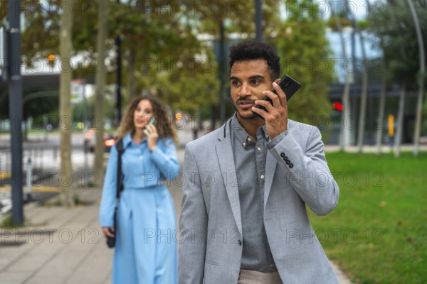 Business colleagues walking on a city sidewalk while communicating on their mobile phones, focusing on professional interaction and connectivity in an urban environment