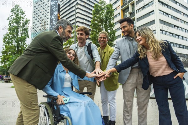 Diverse group of smiling business professionals and an executive in a wheelchair stacking hands, symbolizing teamwork, collaboration, and inclusion in an urban city environment