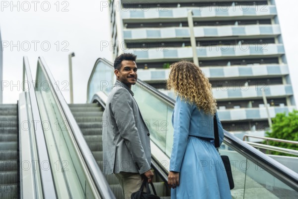 Business partners engaging in a collaborative discussion while commuting on an escalator in a modern city setting, representing urban lifestyle and career growth