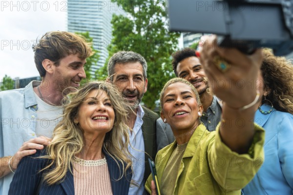 Diverse group of smiling business people and colleagues enjoying a moment together, taking a selfie outdoors in an urban setting with modern buildings in the background