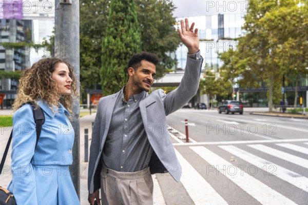 Young businessman hails a taxi on a busy downtown sidewalk while his female colleague stands beside him, both in smart casual attire amid modern city architecture and traffic