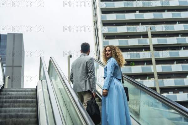 Two diverse business colleagues ascending an escalator, looking towards a modern city building, symbolizing career growth, collaboration, and urban professional life with focus and determination