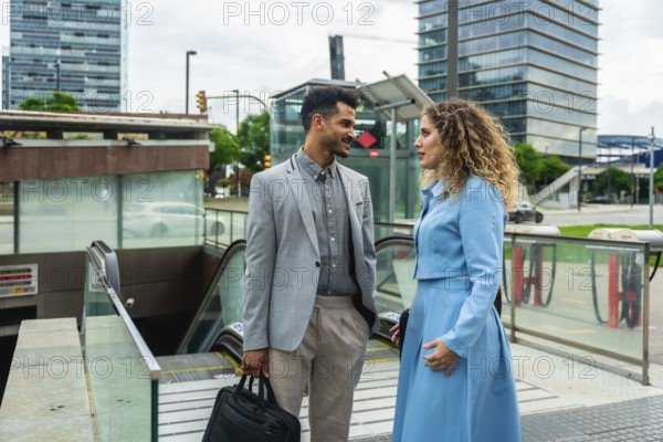 Two business colleagues having a casual conversation while standing near the entrance to an urban subway station with escalators, reflecting professional communication and city life