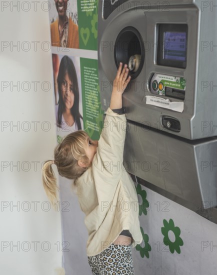 Blond girl, 5 years old, earns pocket money by recycling cans in recycling machine in Ystad, Skåne County, Sweden, Scandinavia
