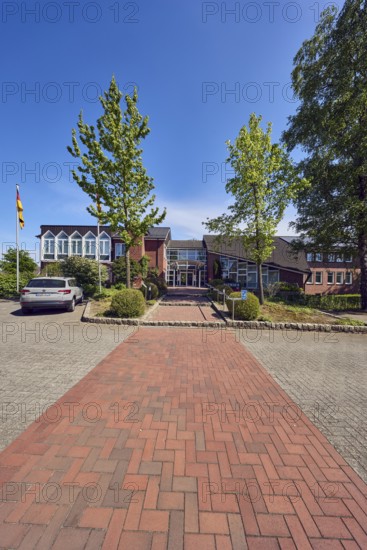 Town hall of the municipality of Neuenkirchen-Vörden, commercial building, modern architecture, parking lot with car, flagpoles, flags, paving walkway, concrete paving street, trees, blue sky, cirrus clouds, Küsterstraße, Neuenkirchen-Vörden district, Vechta district, Lower Saxony, Germany