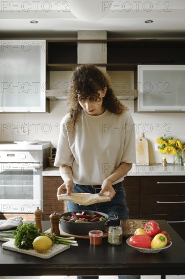 Woman lay down fresh hake fillet over vegetables in a frying pan